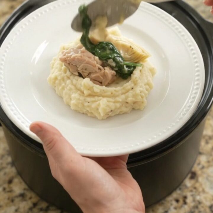 Creamy Swiss spinach artichoke chicken thighs in a slow cooker, topped with melted cheese and steam rising.