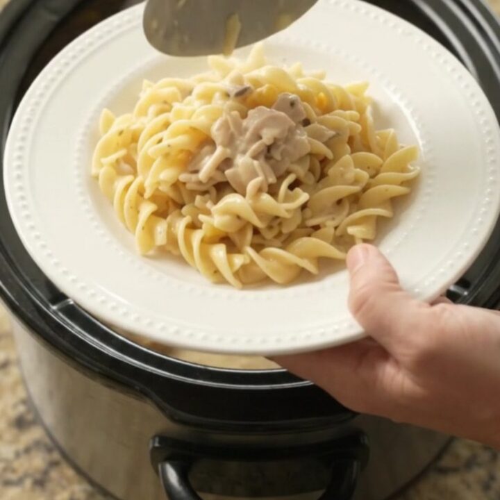 Slow cooker full of creamy Parmesan sweet corn chicken thighs, with a spoon lifting a saucy bite.