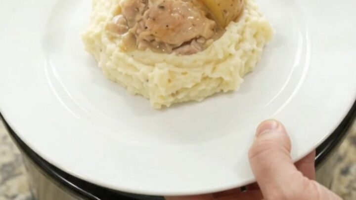 A slow cooker filled with creamy Swiss chicken and baby potatoes, with a spoon lifting a bite.