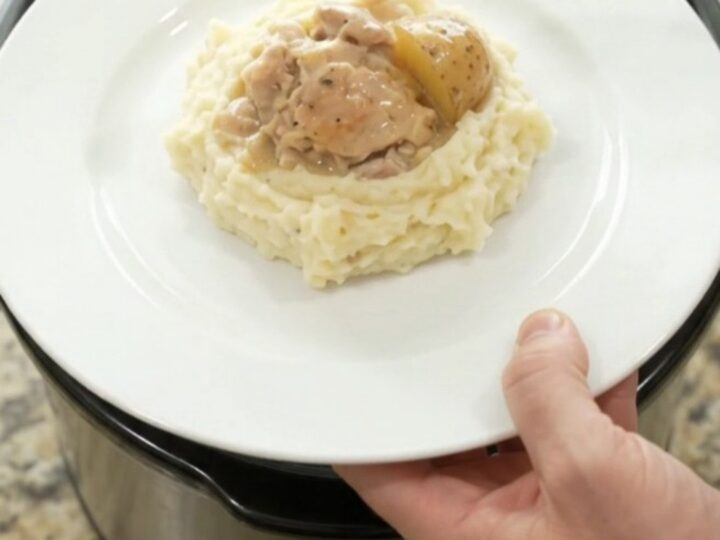 A slow cooker filled with creamy Swiss chicken and baby potatoes, with a spoon lifting a bite.