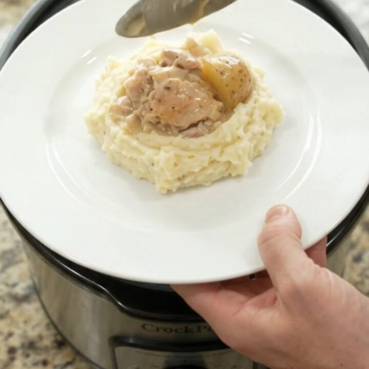 A slow cooker filled with creamy Swiss chicken and baby potatoes, with a spoon lifting a bite.