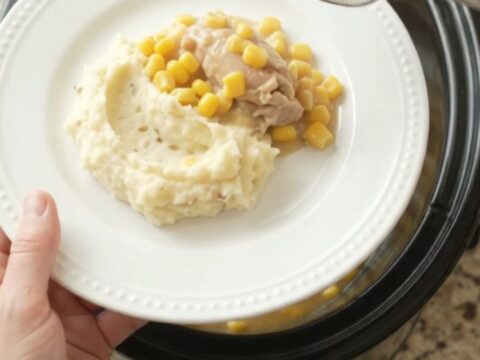 A slow cooker filled with creamy Swiss sweet corn chicken thighs, with a spoon lifting a steaming scoop.