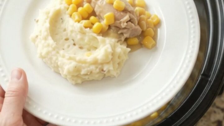 A slow cooker filled with creamy Swiss sweet corn chicken thighs, with a spoon lifting a steaming scoop.
