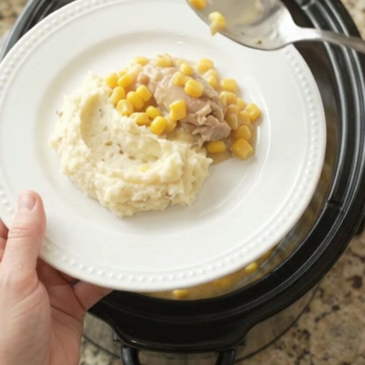 A slow cooker filled with creamy Swiss sweet corn chicken thighs, with a spoon lifting a steaming scoop.