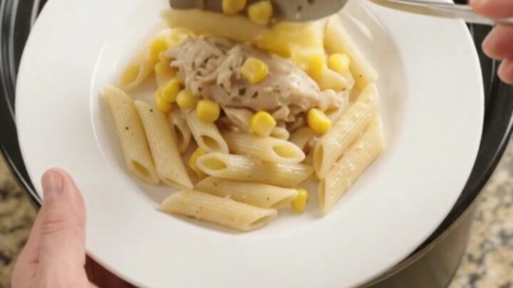 A slow cooker filled with creamy chicken and corn, topped with melted mozzarella, steam rising