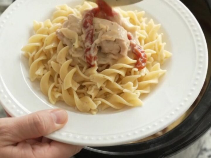 Creamy slow cooker chicken thighs with sun-dried tomatoes and Parmesan sauce, served over buttered noodles