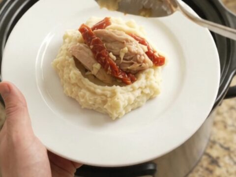 Creamy Swiss sun-dried tomato chicken thighs simmering in a slow cooker, topped with melted cheese and herbs.