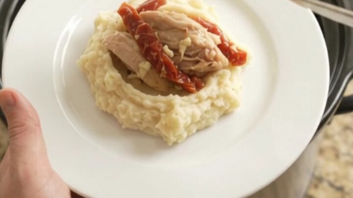 Creamy Swiss sun-dried tomato chicken thighs simmering in a slow cooker, topped with melted cheese and herbs.