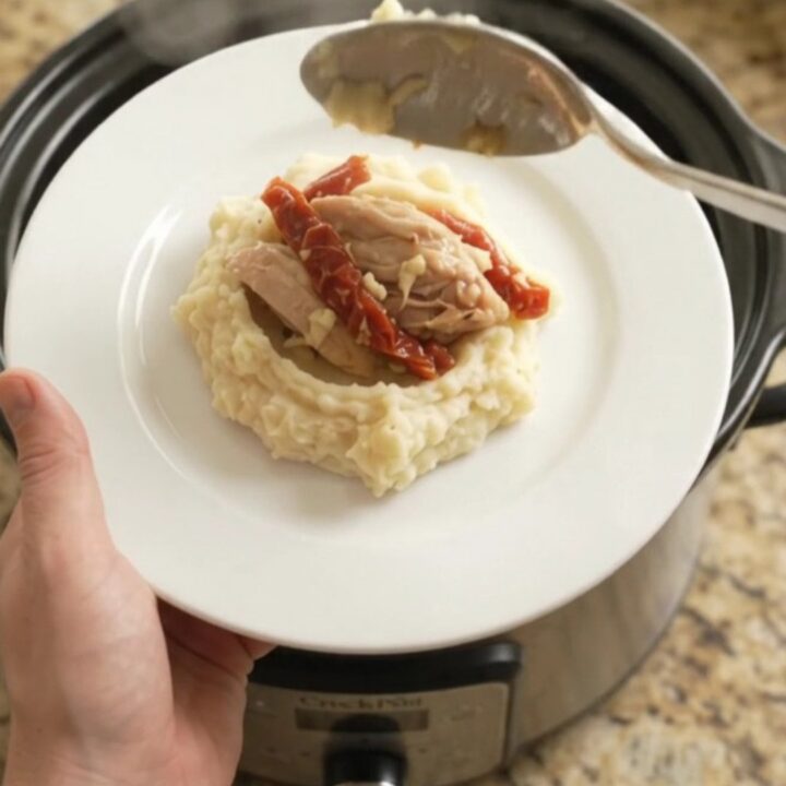 Creamy Swiss sun-dried tomato chicken thighs simmering in a slow cooker, topped with melted cheese and herbs.
