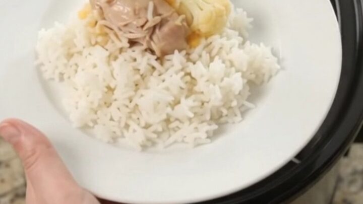 Slow cooker filled with creamy cheddar chicken and cauliflower, with a spoon lifting a saucy bite