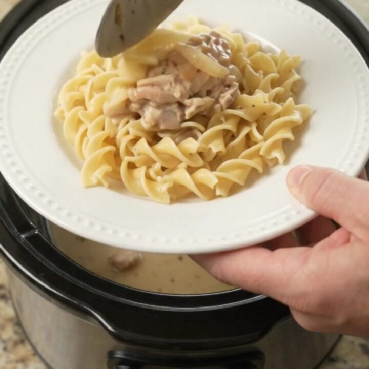 Creamy Parmesan French onion chicken thighs in a slow cooker, topped with sweet onions and a velvety white sauce.