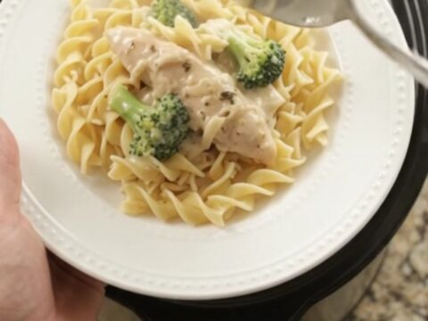 Slow cooker full of creamy Parmesan broccoli chicken tenders, with a spoon lifting a saucy bite.