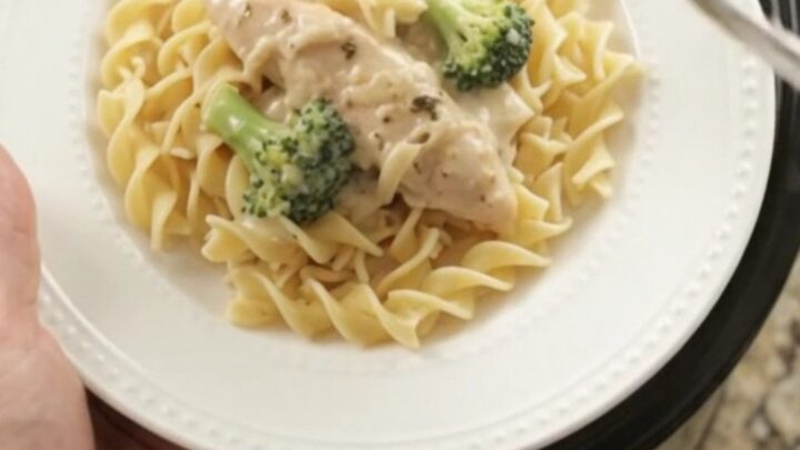 Slow cooker full of creamy Parmesan broccoli chicken tenders, with a spoon lifting a saucy bite.