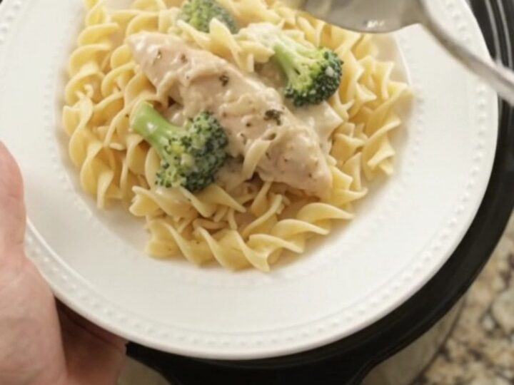 Slow cooker full of creamy Parmesan broccoli chicken tenders, with a spoon lifting a saucy bite.