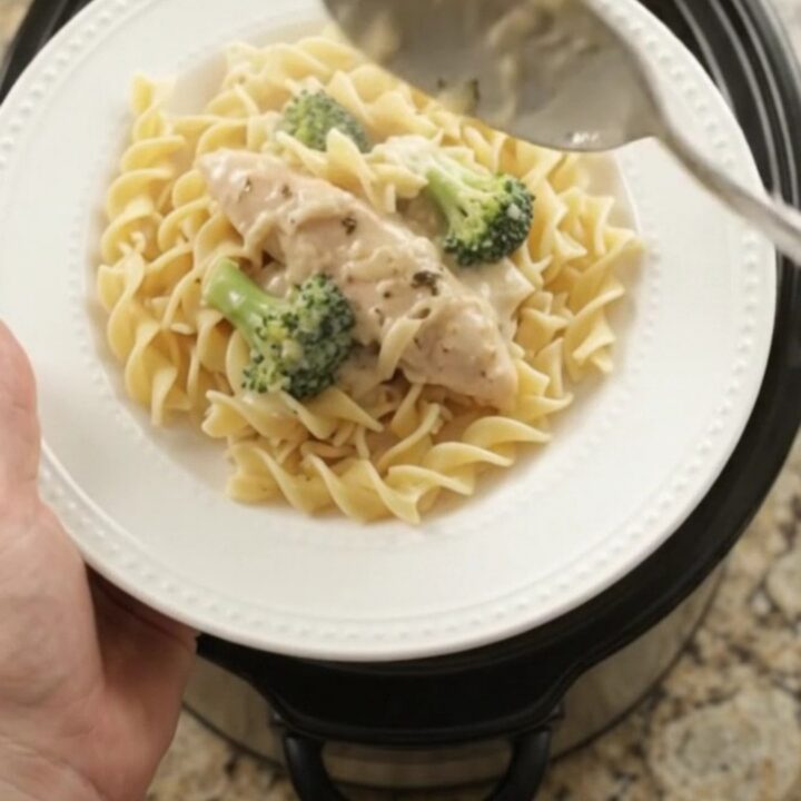 Slow cooker full of creamy Parmesan broccoli chicken tenders, with a spoon lifting a saucy bite.