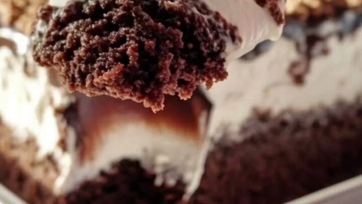 A close-up of a silver spoon scooping into a decadent chocolate cake topped with whipped cream and fudge.