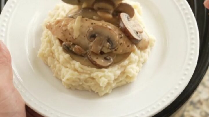 Slow cooker filled with creamy Swiss mushroom chicken, topped with melted cheese and herbs.