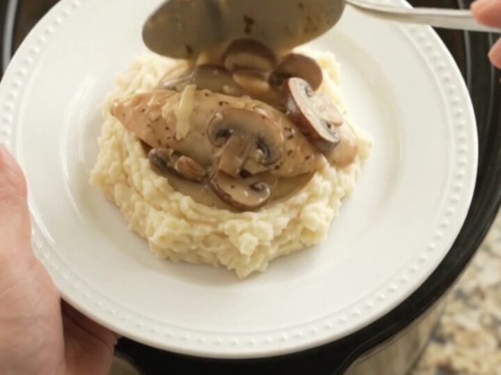 Slow cooker filled with creamy Swiss mushroom chicken, topped with melted cheese and herbs.