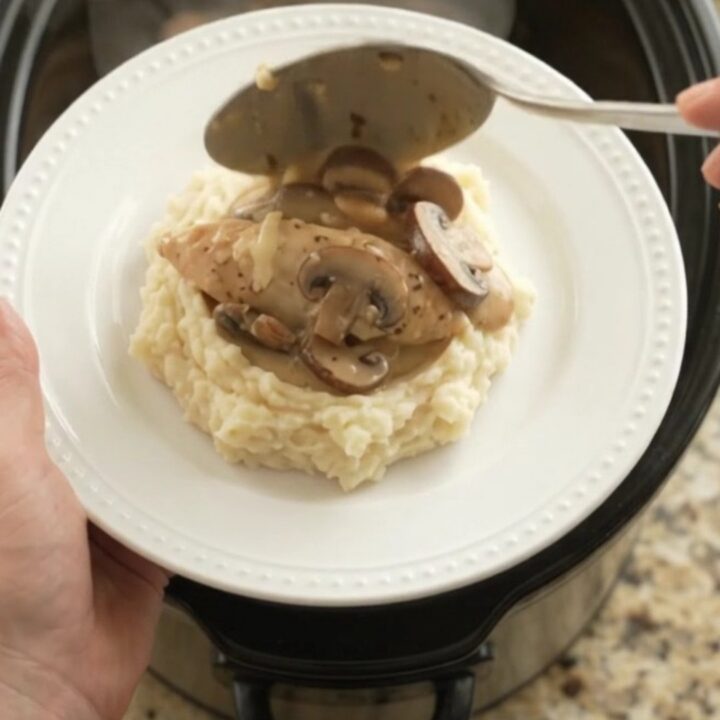 Slow cooker filled with creamy Swiss mushroom chicken, topped with melted cheese and herbs.