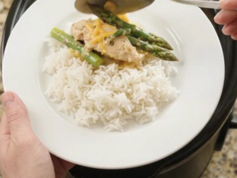 Slow cooker cheddar asparagus chicken tenders in a black crockpot, bubbling with creamy yellow sauce