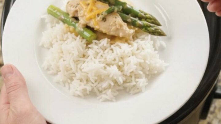 Slow cooker cheddar asparagus chicken tenders in a black crockpot, bubbling with creamy yellow sauce