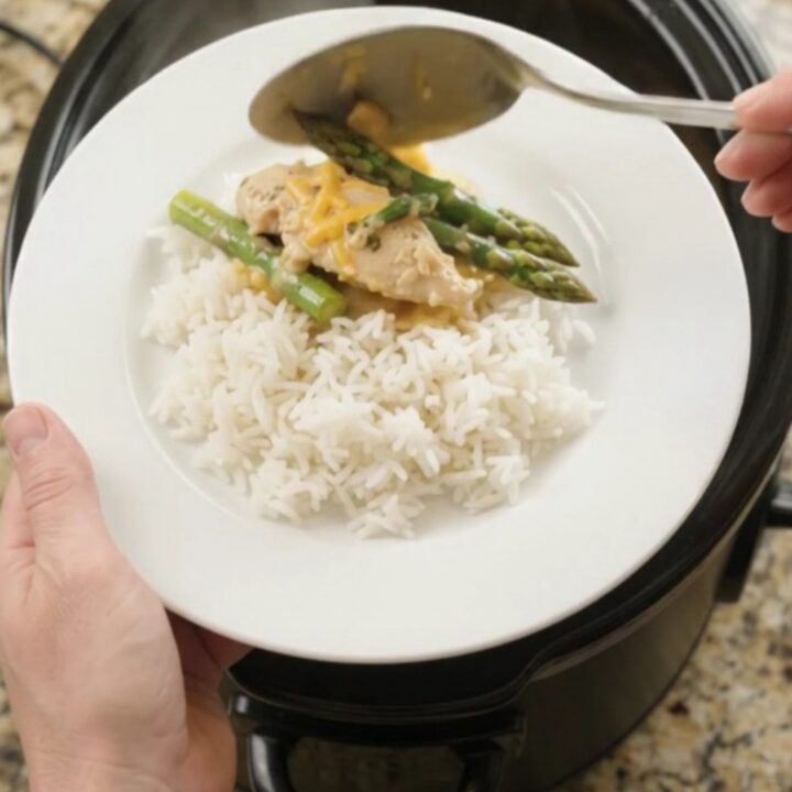 Slow cooker cheddar asparagus chicken tenders in a black crockpot, bubbling with creamy yellow sauce