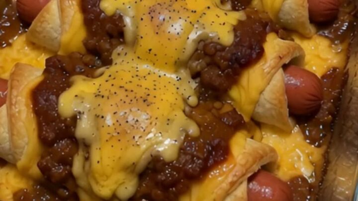 A close-up of a chili cheese dog crescent roll being lifted, showing melted cheddar and savory chili.