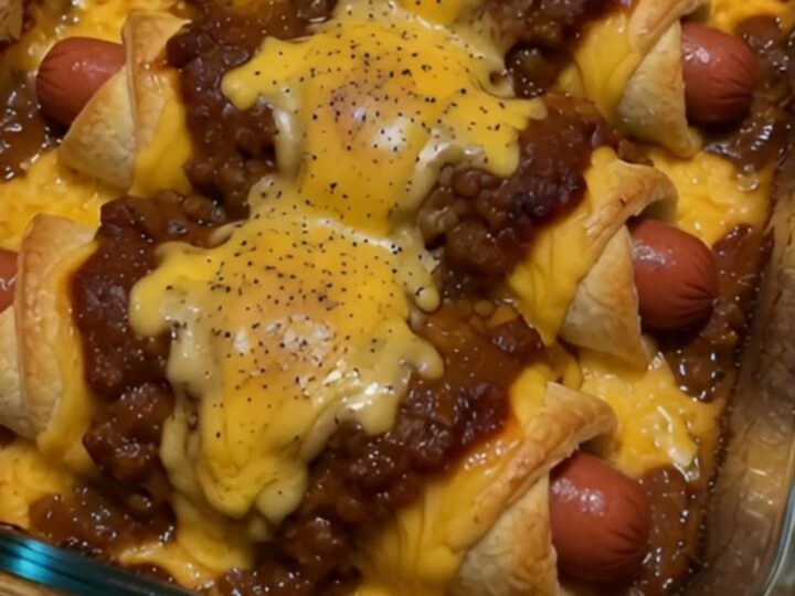 A close-up of a chili cheese dog crescent roll being lifted, showing melted cheddar and savory chili.