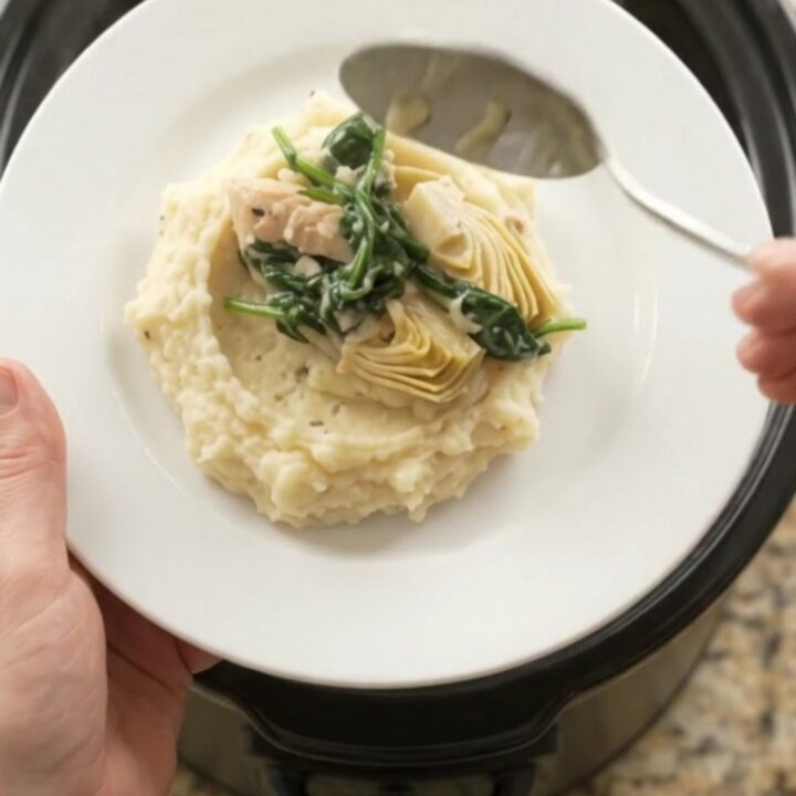 Slow cooker filled with creamy Swiss spinach artichoke chicken tenders, bubbling and steaming