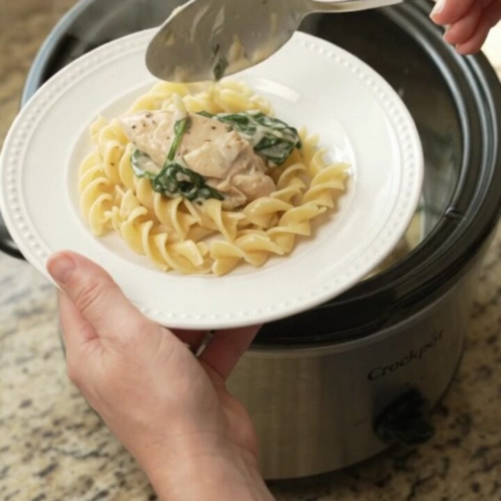 Creamy Crockpot chicken with spinach and artichokes in a white bowl