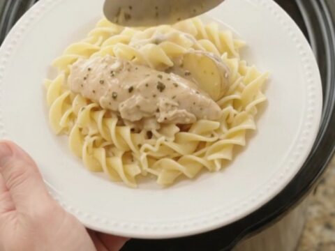 A slow cooker filled with creamy Parmesan chicken and potatoes, with a spoon lifting a generous scoop.