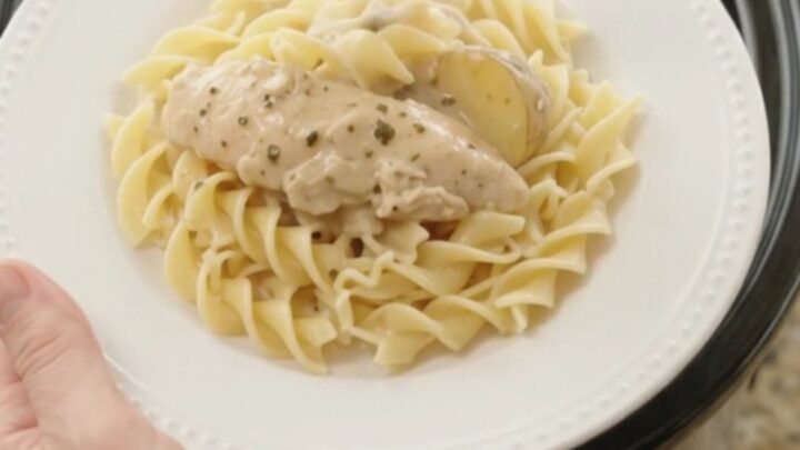 A slow cooker filled with creamy Parmesan chicken and potatoes, with a spoon lifting a generous scoop.
