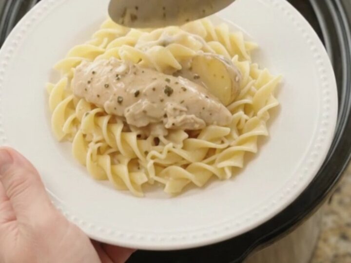 A slow cooker filled with creamy Parmesan chicken and potatoes, with a spoon lifting a generous scoop.