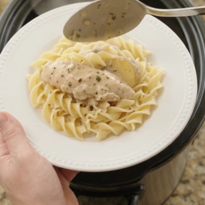 A slow cooker filled with creamy Parmesan chicken and potatoes, with a spoon lifting a generous scoop.