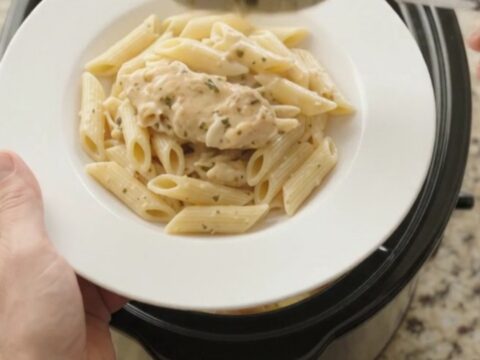 Slow cooker chicken and potatoes with creamy sauce, topped with melted cheese.