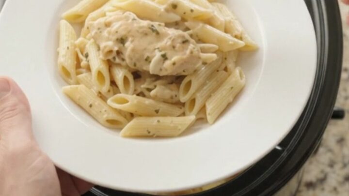 Slow cooker chicken and potatoes with creamy sauce, topped with melted cheese.