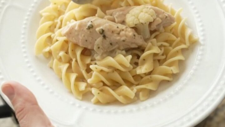 A slow cooker filled with creamy chicken and cauliflower, topped with melted cheese and steam rising