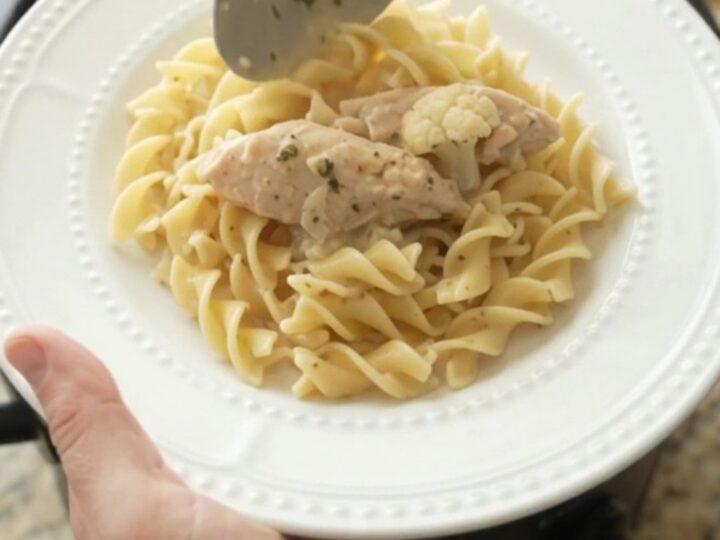 A slow cooker filled with creamy chicken and cauliflower, topped with melted cheese and steam rising