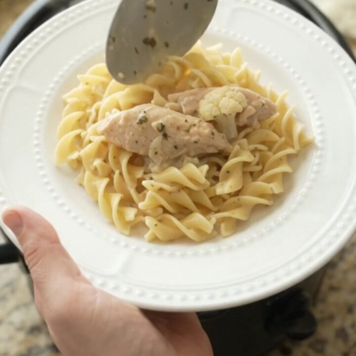 A slow cooker filled with creamy chicken and cauliflower, topped with melted cheese and steam rising