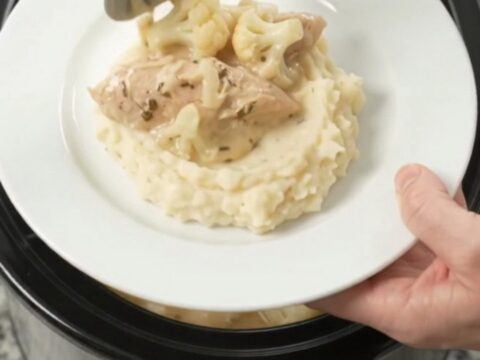 Slow cooker filled with creamy Swiss cauliflower chicken tenders, garnished with fresh herbs