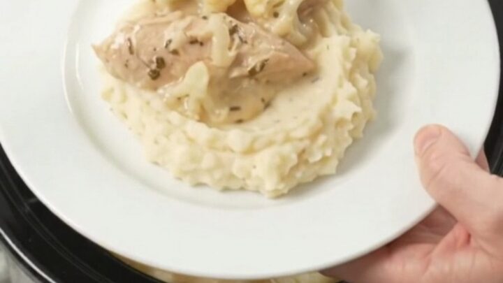 Slow cooker filled with creamy Swiss cauliflower chicken tenders, garnished with fresh herbs