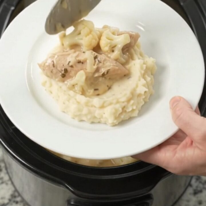 Slow cooker filled with creamy Swiss cauliflower chicken tenders, garnished with fresh herbs