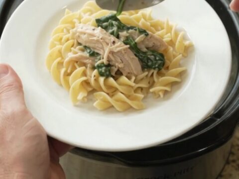 Creamy slow cooker turkey with spinach and artichokes in a white bowl, topped with Parmesan