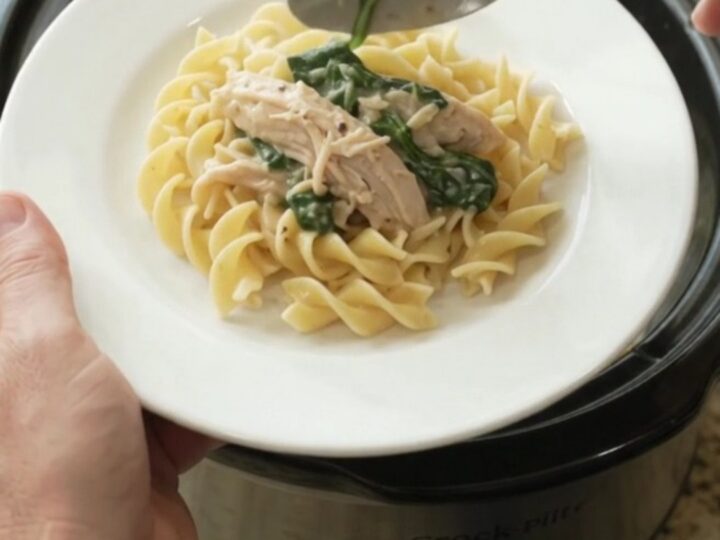 Creamy slow cooker turkey with spinach and artichokes in a white bowl, topped with Parmesan