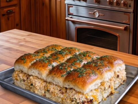 A close-up of cheesy chicken bacon sliders on a metal pan in a rustic kitchen.