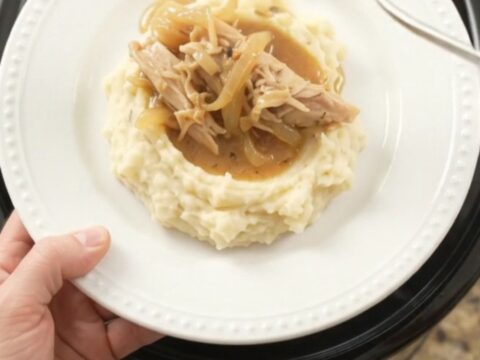 A slow cooker filled with creamy Swiss French Onion Turkey Breast, topped with melted cheese and caramelized onions.