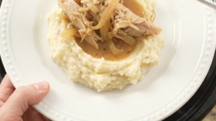 A slow cooker filled with creamy Swiss French Onion Turkey Breast, topped with melted cheese and caramelized onions.