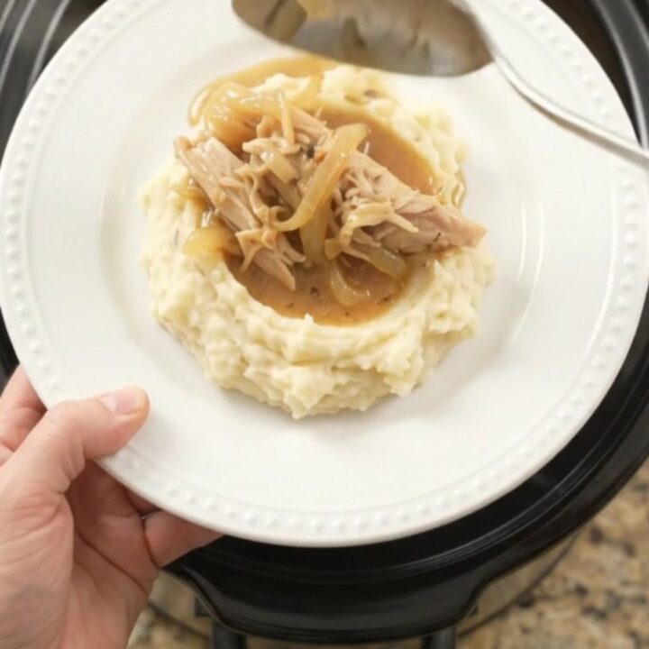 A slow cooker filled with creamy Swiss French Onion Turkey Breast, topped with melted cheese and caramelized onions.