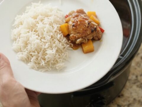 Slow-cooker mango honey soy chicken thighs in a black crockpot, topped with mango cubes and red peppers