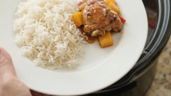 Slow-cooker mango honey soy chicken thighs in a black crockpot, topped with mango cubes and red peppers